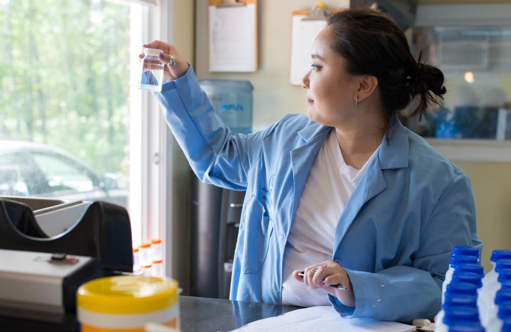 A student takes notes while holding up a small bottle of clear liquid